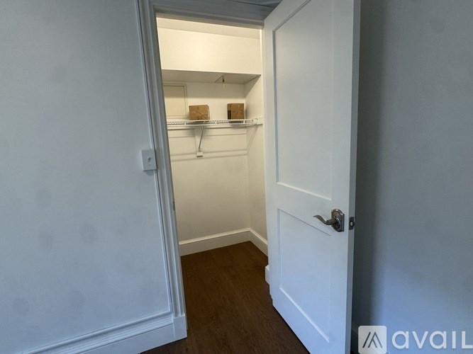 A white door is open to a small pantry with shelves and boxes.