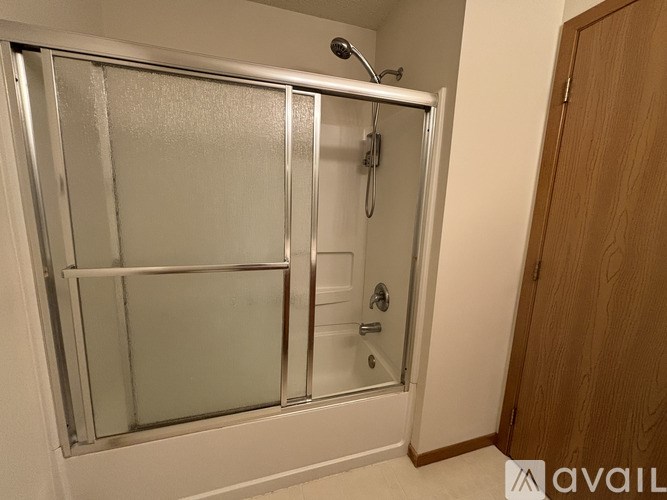A shower with a glass door and a wooden door to the right.