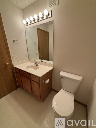 A bathroom with a toilet, sink, mirror, and lights.
