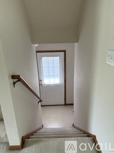 A staircase with a carpeted runner leads up to a white door.