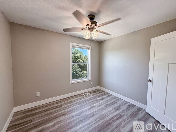 A room with a ceiling fan and a window overlooking a green area.