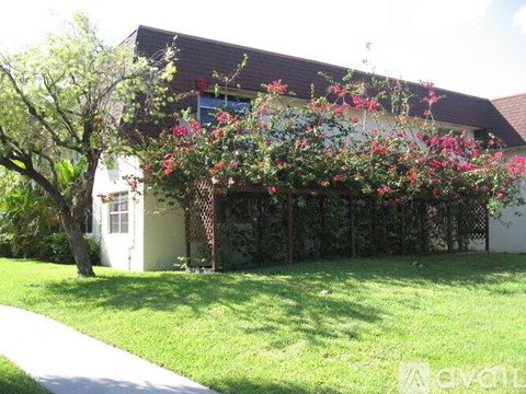 A white house with a tree and flowers in front.
