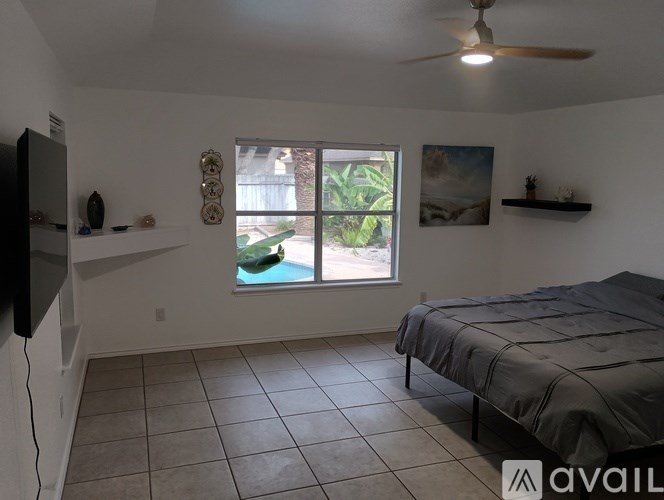 A bedroom with a bed, a ceiling fan, and a window with a view of a garden.