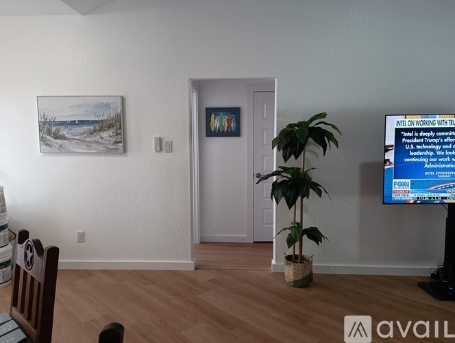 A living room with a television on, a plant, and a painting on the wall.
