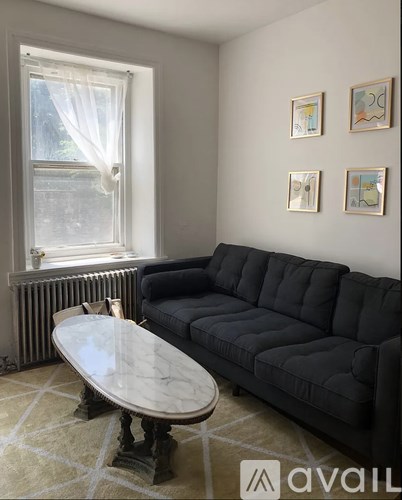 A black couch sits in a living room with a round table in front of it.