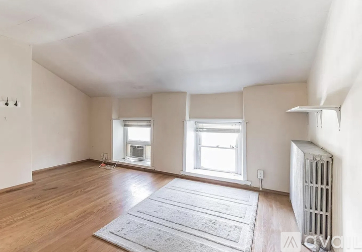 A spacious room with wooden floors and two windows.