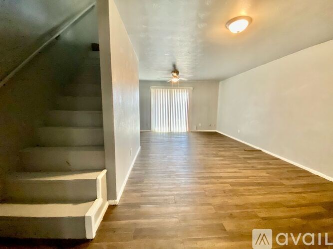 A spacious room with wooden flooring and a staircase on the left side.