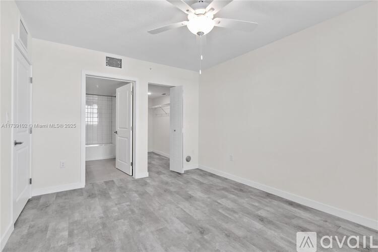 A spacious room with a ceiling fan and light, and a doorway leading to another room.