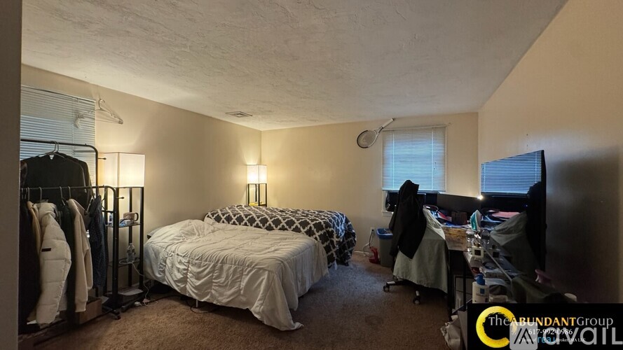 A bedroom with a bed, a desk, and a clothing rack.