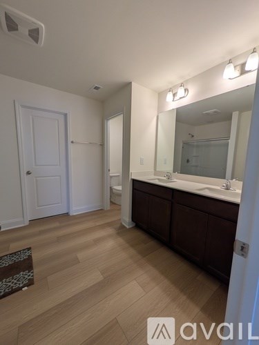 A bathroom with a white door, a mirror, and a wooden floor.