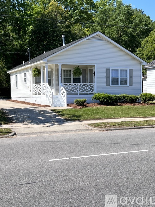 A small white house with a porch and a tree in the background.