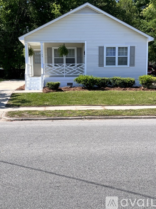 A small white house with a porch and a green lawn in front.