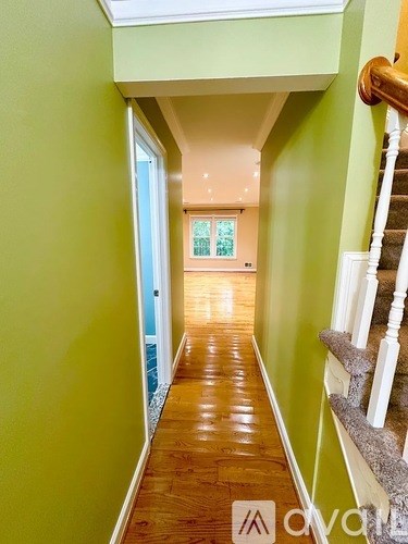 A hallway with green walls and wooden floors leading to a door.