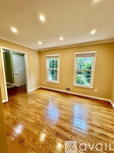 A room with wooden flooring and two windows.