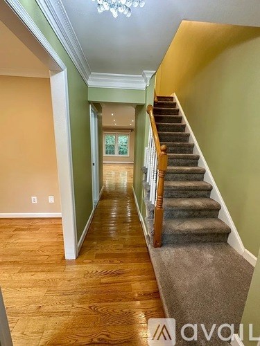 A hallway with wooden floors and a staircase with a carpeted landing.