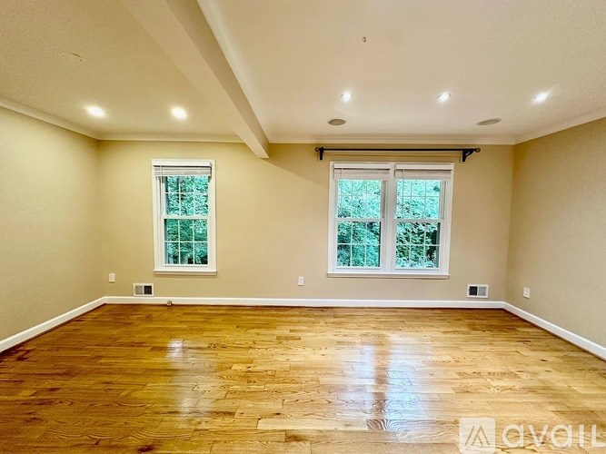 A spacious room with wooden floors and two windows.