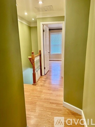 A hallway with green walls and wooden floors leading to a door.