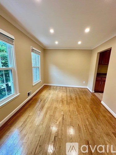 A room with wooden flooring and two windows.