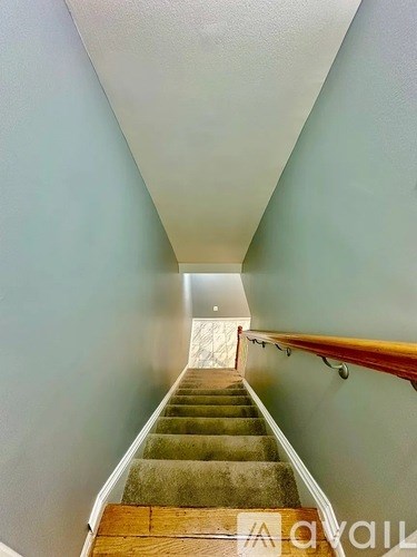 A stairway with a wooden handrail and green carpeted steps.