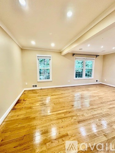 A room with wooden flooring and two windows.