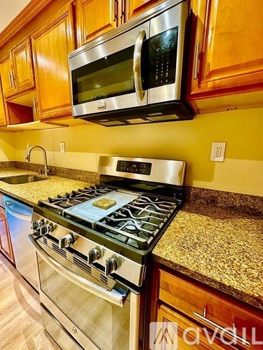 A stainless steel oven with a stove top sits in a kitchen with wooden cabinets.