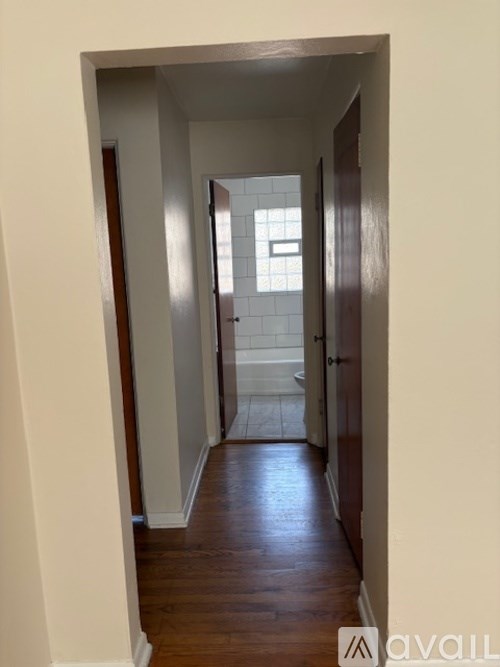 A hallway with wooden floors and white walls leading to a bathroom.
