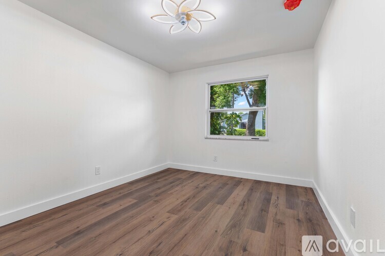 A room with wooden flooring and a window showing trees outside.