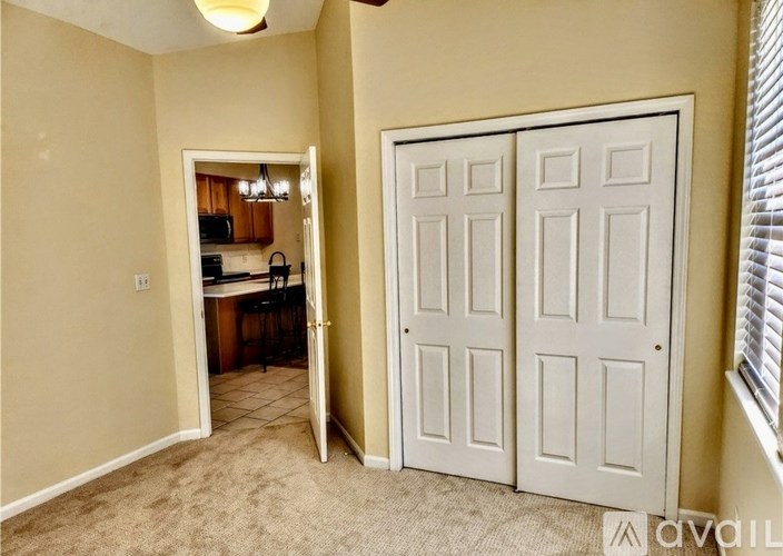 A room with a white door and a kitchen in the background.