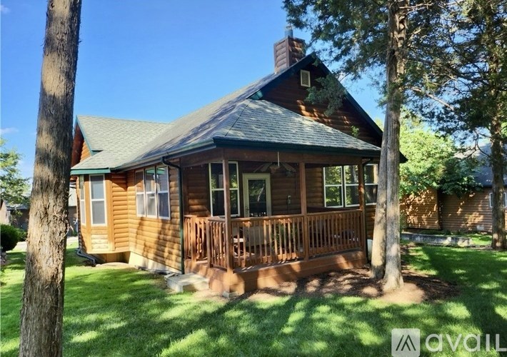 A house with a porch and a chimney is surrounded by trees.