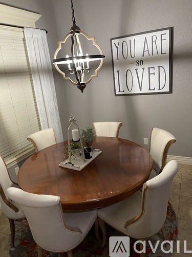 A dining room with a wooden table and chairs, a chandelier, and a sign that says "You are so loved".