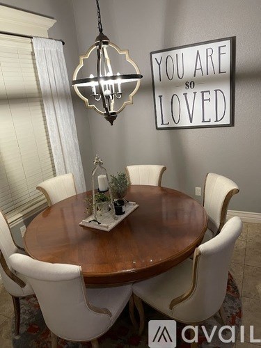A dining room with a wooden table and chairs, a chandelier, and a sign that says "You are so loved".