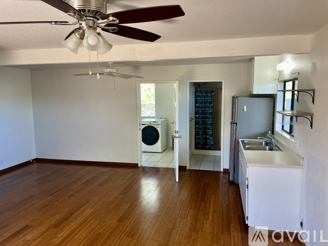 A room with a ceiling fan and a kitchen area with a sink and a refrigerator.