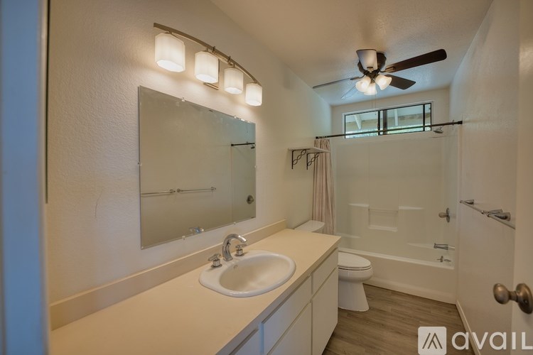 A bathroom with a sink, mirror, toilet, and a fan.