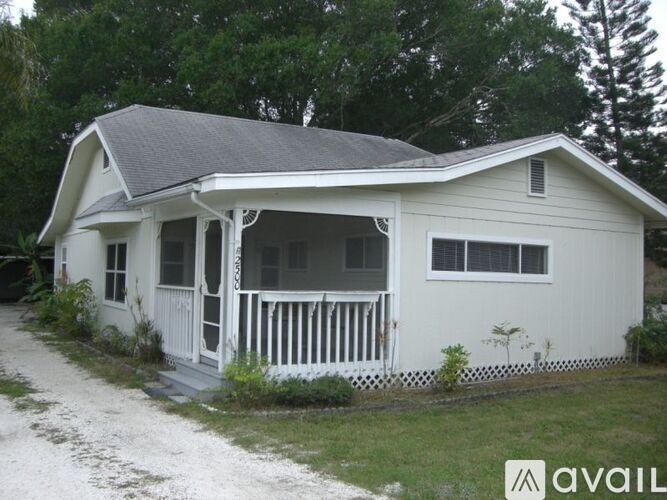 A white house with a porch and a dirt path leading to it.