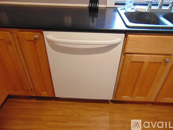 A white dishwasher is in a kitchen with wooden cabinets.