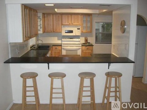 A kitchen with wooden cabinets and a black countertop with three stools.