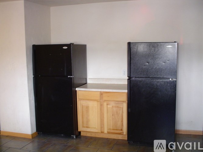 Two black refrigerators in a room with a wooden cabinet.