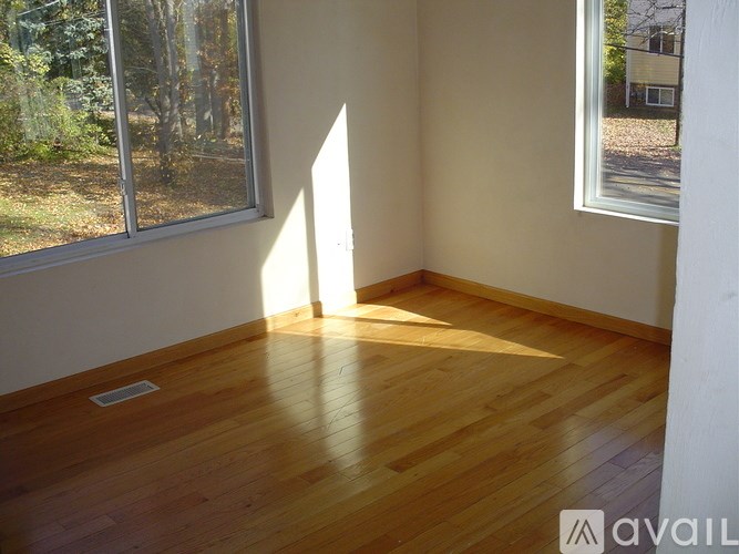 A room with wooden flooring and two windows letting in sunlight.