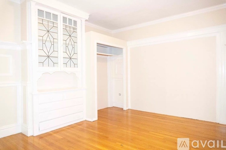 A room with wooden floors and white walls, with a window and a door visible.