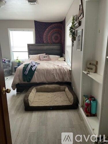 A bedroom with a bed, a dog bed, and a wall hanging.