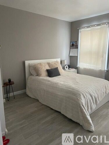 A bedroom with a large bed and a window with white curtains.
