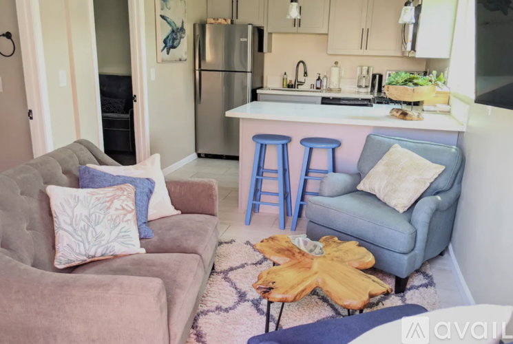 A kitchen with a refrigerator, a sink, and a countertop with a blue chair and a couch with a pillow on it.