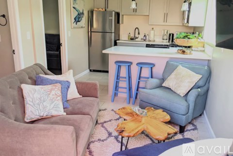A kitchen with a refrigerator, a sink, and a countertop with a blue chair and a couch with a pillow on it.