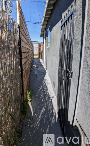 A narrow alley with a wooden fence on the left and a grey building on the right.