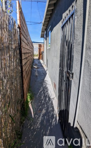 A narrow alley with a wooden fence on the left and a grey building on the right.
