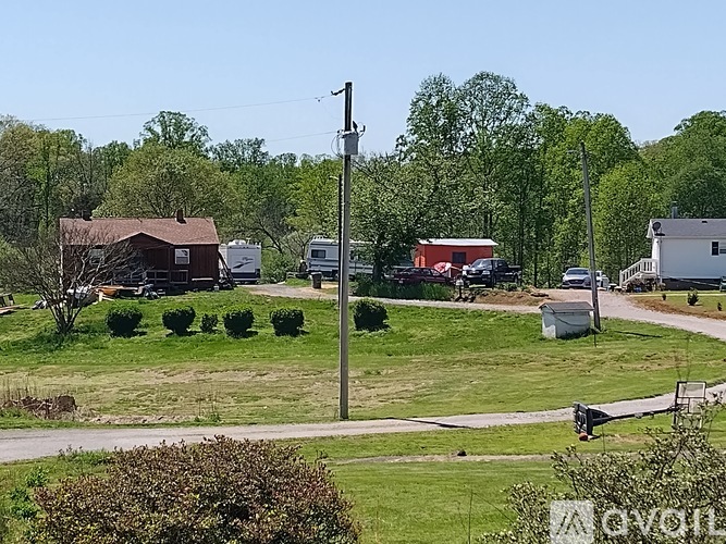 A rural landscape with a house, trees, and a utility pole.
