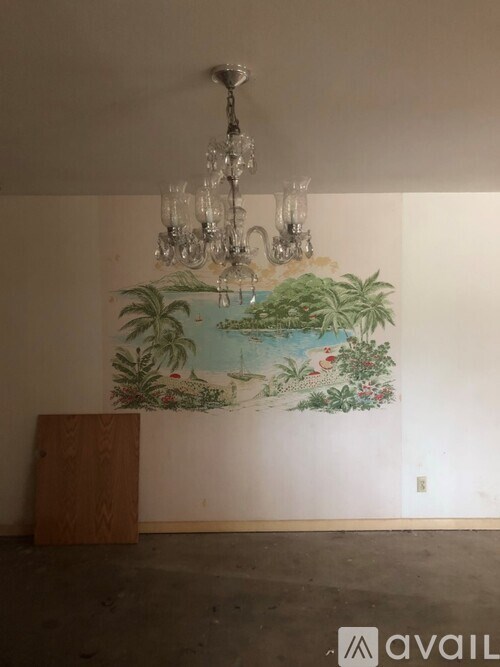 A room with a chandelier and a painting of a tropical scene on the wall.