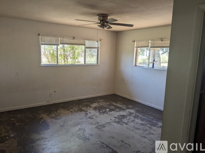 A dirt path leads through a wooded area with a fence and a building in the background.