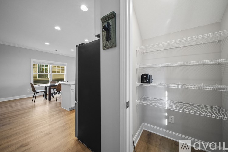 A black refrigerator stands in a kitchen with a dining table and chairs in the background.