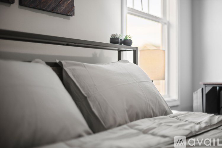 A bed with white pillows and a grey comforter in a room with a window.